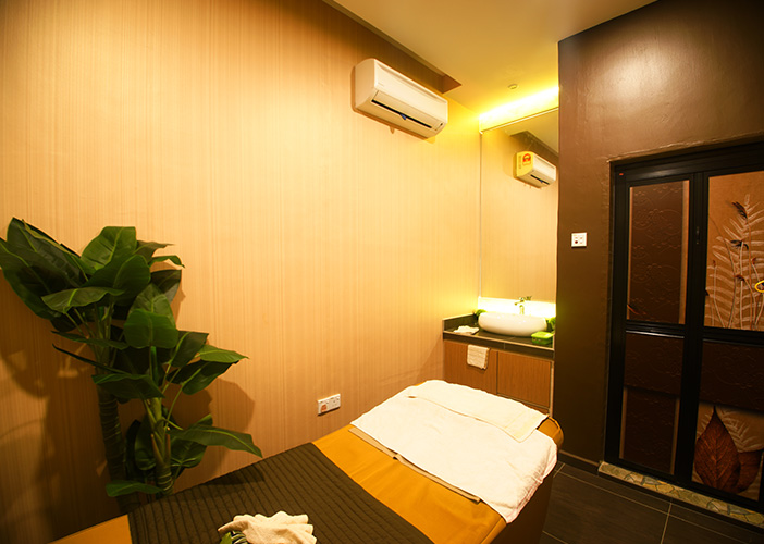 Small treatment room with a bed covered in white linens, sink area, and a potted plant, calm and clean mood