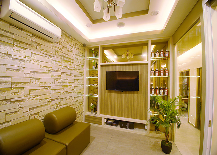 Small lounge room with stone accent wall, wall-mounted TV, shelving with bottles, leather bench seating and a potted plant